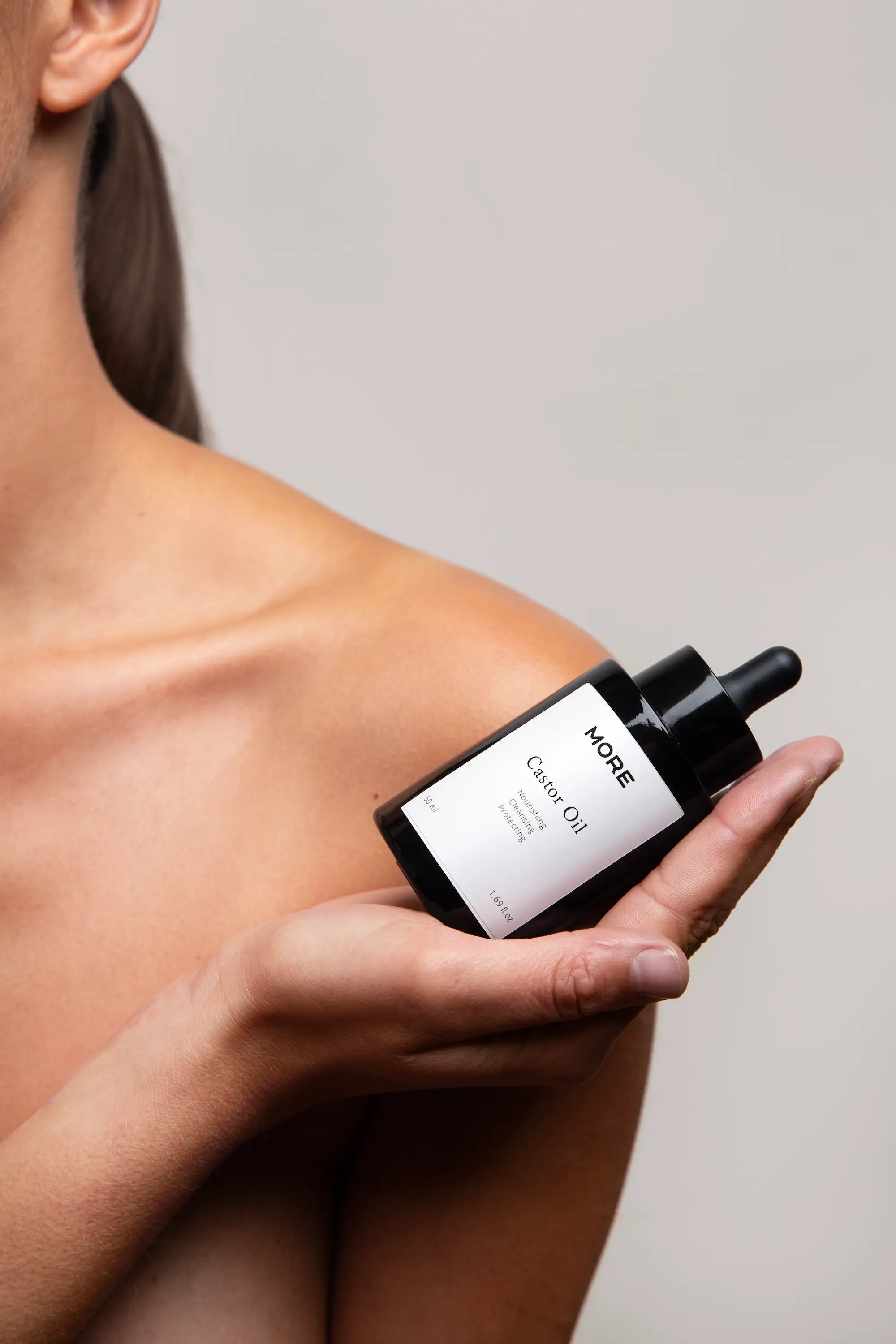 Model houdt More Natural Castor Oil 50 ml vast voor huid en haarverzorging